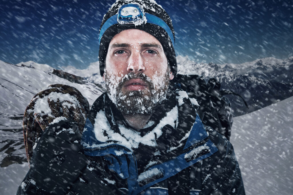 Porträt eines Mannes in warmer Outdoorkleidung im Schnee vor einem Bergpanorama