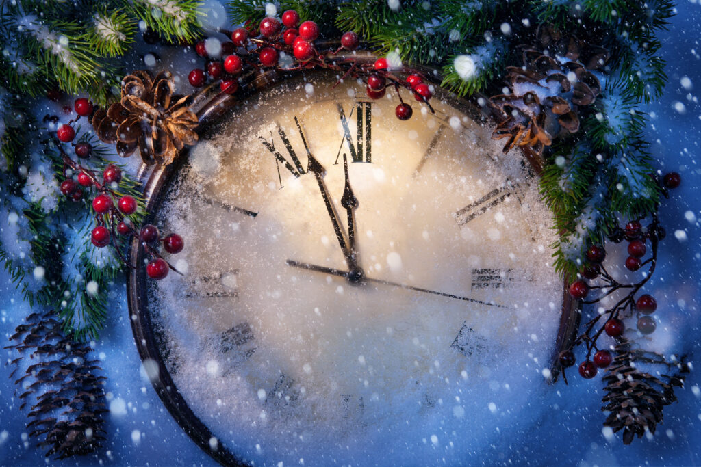 Verschneite und weihnachtlich dekorierte Uhr zeigt kurz vor zwölf Uhr an.