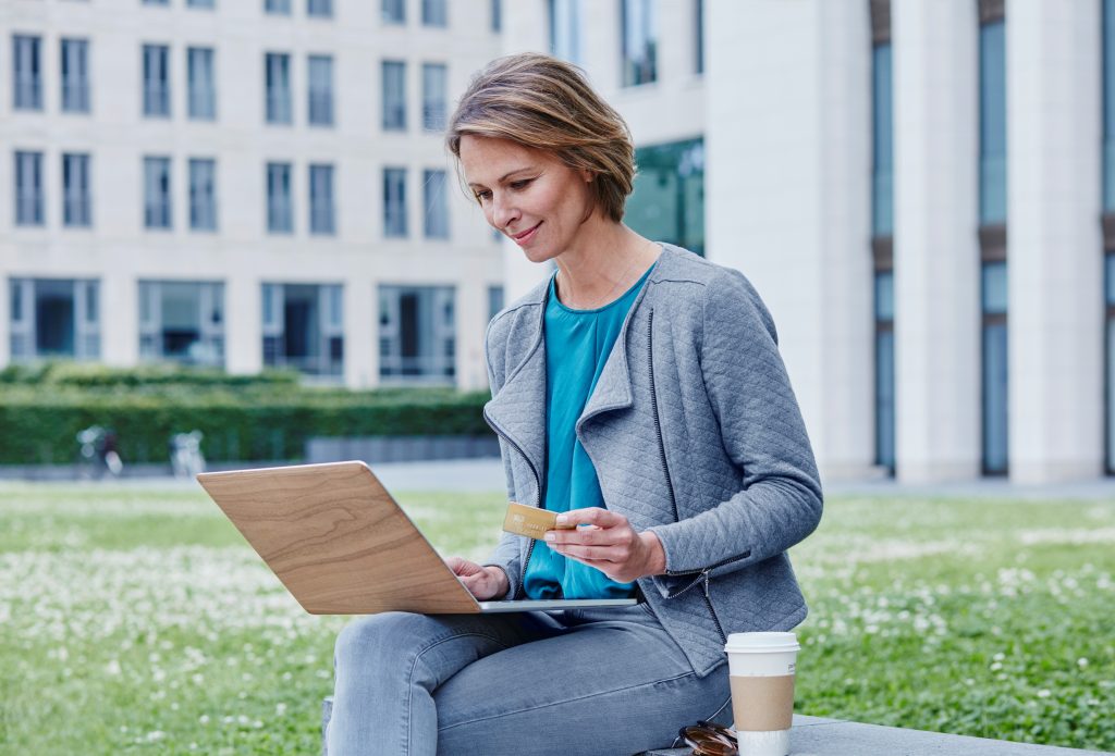 Woman outdoors with laptop, credit card and takeaway coffee