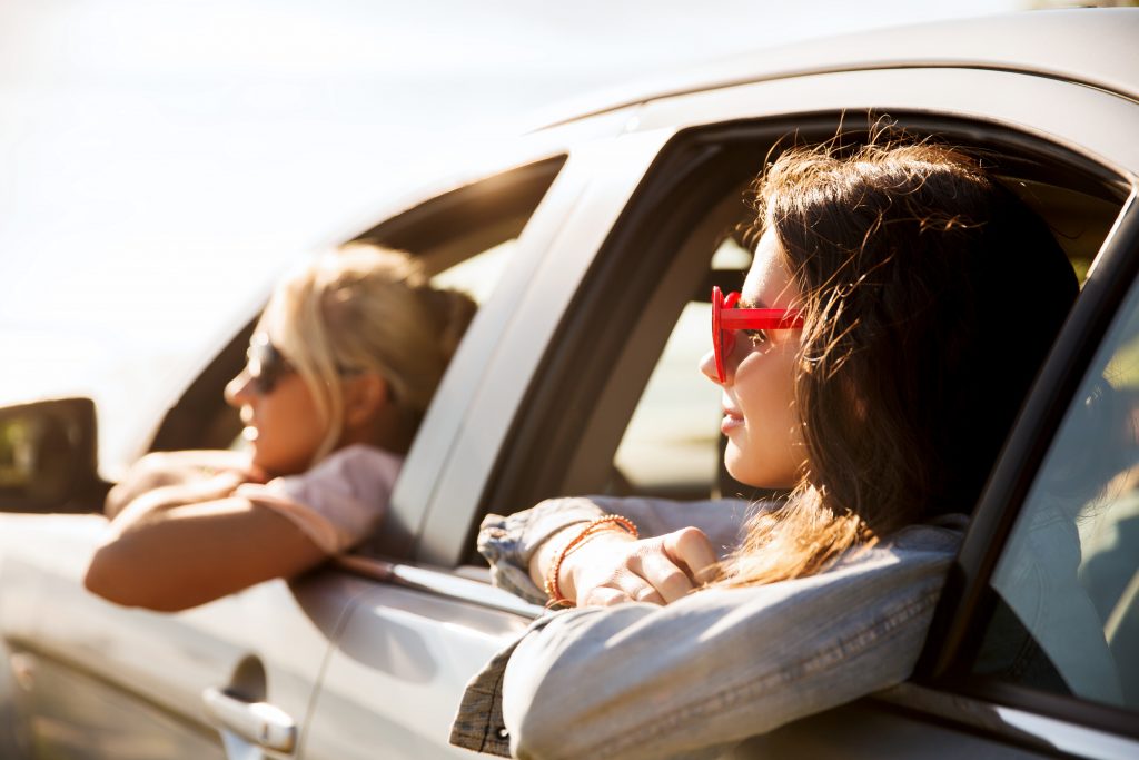 2 Frauen lehnen sich glücklich aus dem Auto heraus und teilen sich ein Auto
