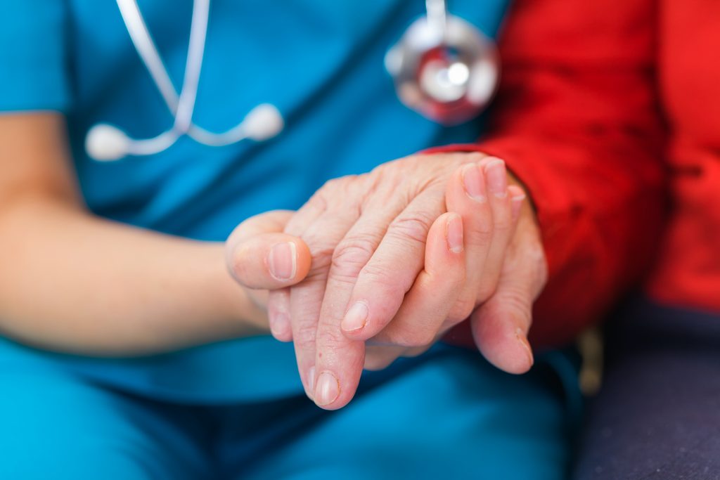 Nahaufnahme eines Sterbebegleiters, der die Hände eines Patienten im Hospiz fest hält