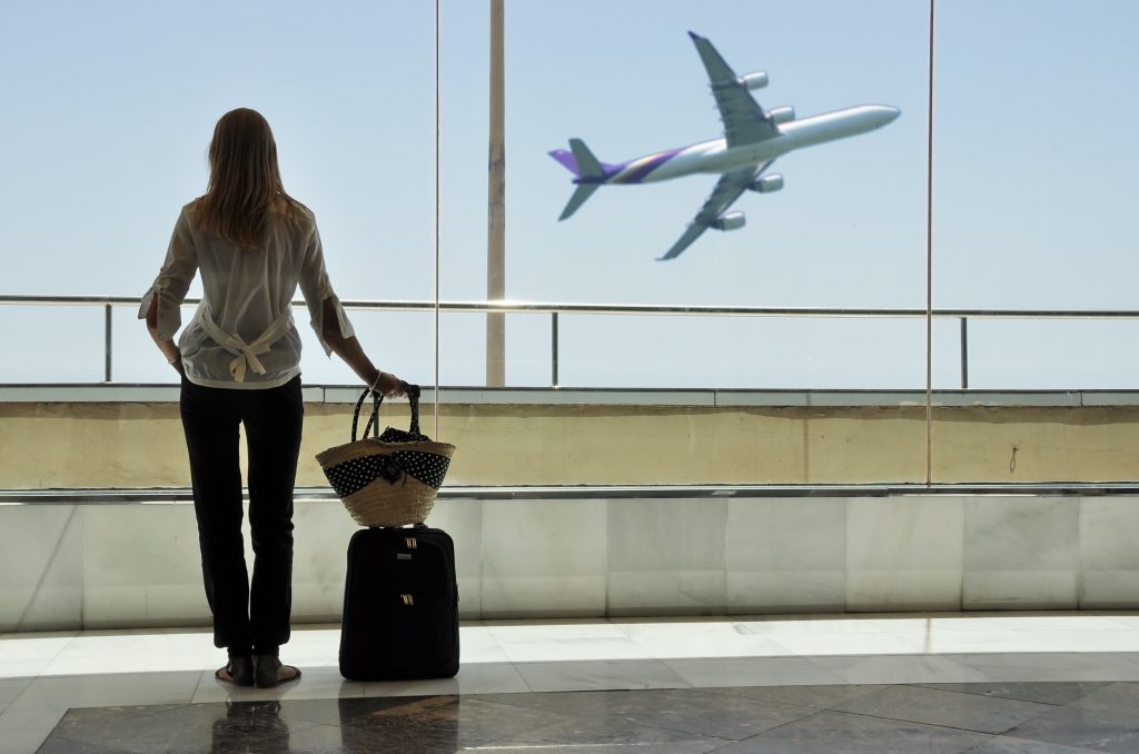 Eine junge Frau steht mit Gepäck am Flughafen und schaut aus dem Fenster