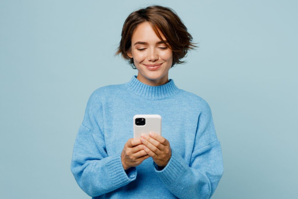 Junge Frau schaut lächelnd auf ihr Smartphone