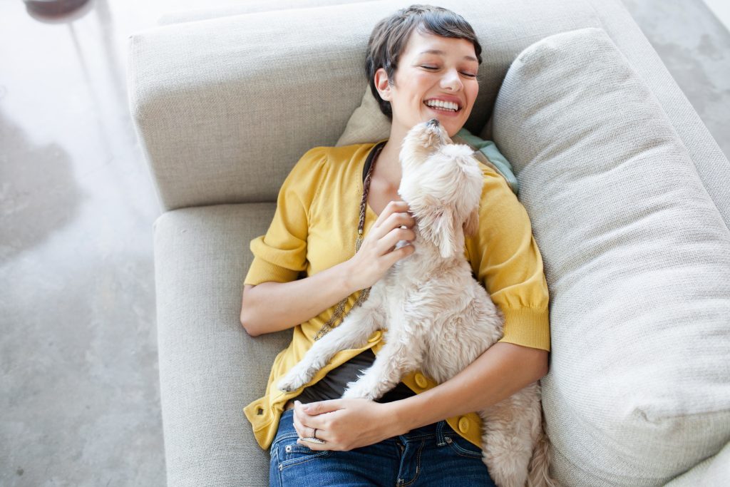 Junge Frau auf einem Wohnzimmersofa umarmt ihren Hund