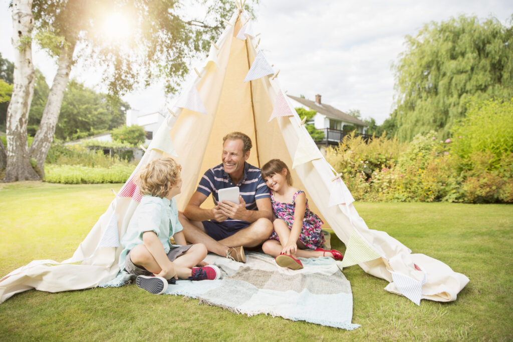 Ein Vater sitzt mit seinen Kindern unter einem Tipi im Garten