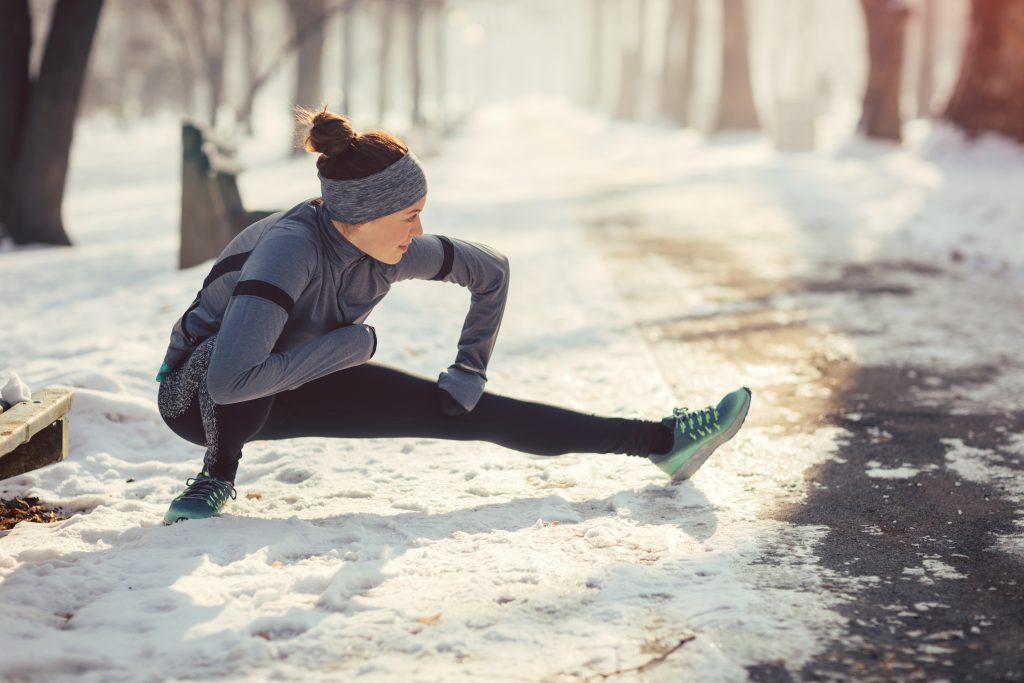 Läuferin in einem verschneiten Wald beim Stretching